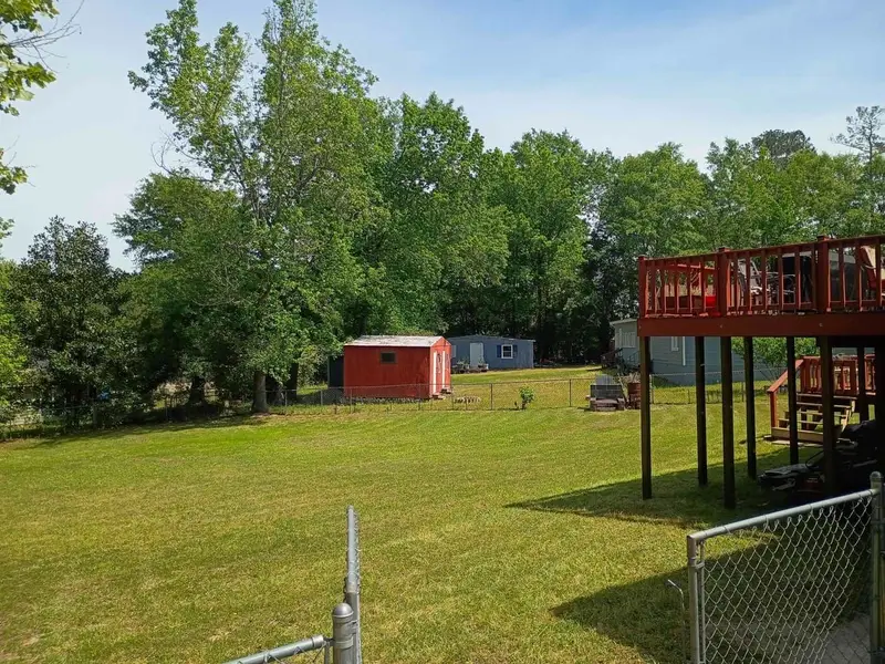 Big fenced backyard mowed short, with a red shed and a raised deck