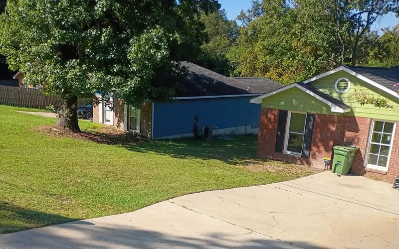 Sloped front lawn mowed under a big shade tree, edged along the driveway